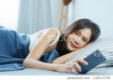 Asian young woman got a phone call on smartphone while sleeping on the bed in morning and trying to ignore incoming phone call. Woman turn off or snooze his alarm clock on smartphone. 116517276