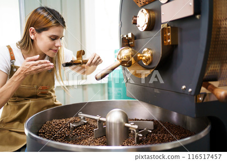 Professional coffee roaster working with modern automated roasting machine in the coffee roasting factory. Food and beverage business concept. Professional coffee roaster working with modern automated roasting machine in the coffee roasting factory. Food and beverage business concept. 116517457