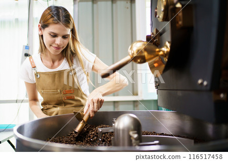 Professional coffee roaster working with modern automated roasting machine in the coffee roasting factory. Food and beverage business concept. Professional coffee roaster working with modern automated roasting machine in the coffee roasting factory. Food and beverage business concept. 116517458