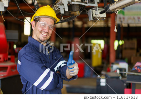 Professional caucasian white ethnicity male technician operating the heavy duty machine in the lathing factory. Technician in safety and helmet suit controlling a machine in factory. 116517618