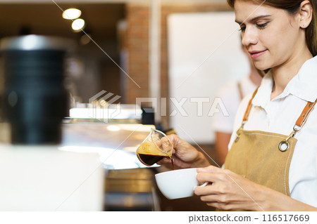 Professional Asian female barista pouring a shot of espresso into a coffee cup close up. Happy female barista making a cup of espresso coffee in a small coffee shop. Small business concept. 116517669