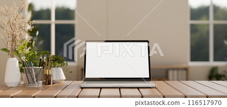 A laptop computer with a white-screen mockup on a wooden table in a contemporary minimalist room. 116517970