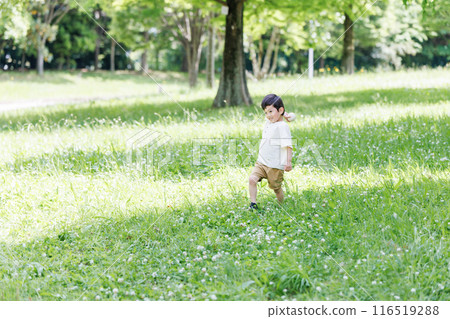 A boy playing energetically in a park with fresh greenery 116519288