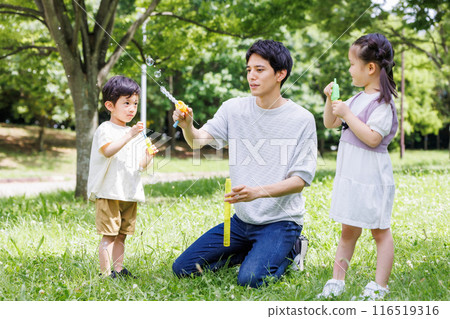 Parents and children playing with soap bubbles in a park with fresh greenery Parents and children playing with soap bubbles in a park with fresh greenery 116519316
