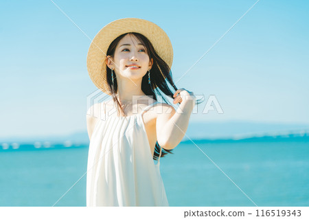 A woman wearing a straw hat with the sea and blue sky in the background A woman wearing a straw hat with the sea and blue sky in the background 116519343