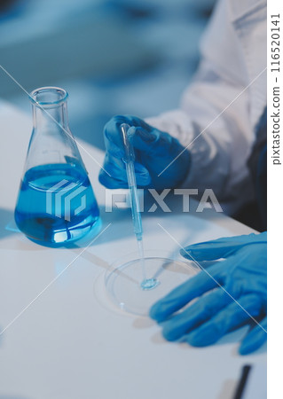 Group of dedicated scientist conduct chemical experiment in medical laboratory, carefully drop precise amount of liquid from pipette into test tube for vaccine drug or antibiotic development. Neoteric 116520141