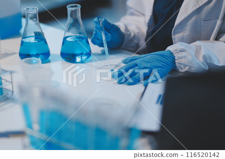 Group of dedicated scientist conduct chemical experiment in medical laboratory, carefully drop precise amount of liquid from pipette into test tube for vaccine drug or antibiotic development. Neoteric 116520142
