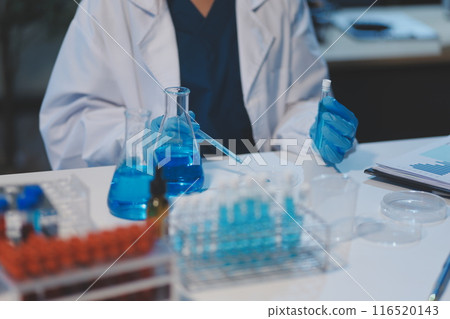 Group of dedicated scientist conduct chemical experiment in medical laboratory, carefully drop precise amount of liquid from pipette into test tube for vaccine drug or antibiotic development. Neoteric 116520143
