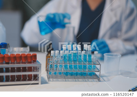 Group of dedicated scientist conduct chemical experiment in medical laboratory, carefully drop precise amount of liquid from pipette into test tube for vaccine drug or antibiotic development. Neoteric 116520147