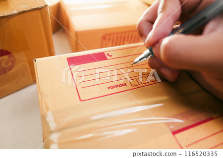 Goods delivery concept Human hand writes an address on a cardboard box for delivery to a customer Goods delivery concept Human hand writes an address on a cardboard box for delivery to a customer 116520335