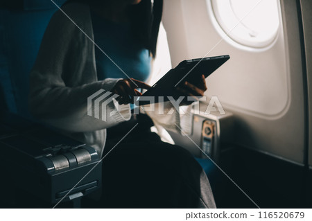 Young asian businesswoman in formal clothes working using tablet with smart pen while sitting in airplane cabin near window traveling to another place 116520679