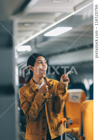 Young Female Tourist with Luggage Walking Through Airplane Cabin Ready for Travel Adventure Young Female Tourist with Luggage Walking Through Airplane Cabin Ready for Travel Adventure 116520766