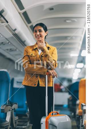 Young Female Tourist with Luggage Walking Through Airplane Cabin Ready for Travel Adventure Young Female Tourist with Luggage Walking Through Airplane Cabin Ready for Travel Adventure 116520768