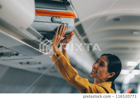 Young Female Tourist Storing Luggage in Overhead Compartment on Airplane During Travel Young Female Tourist Storing Luggage in Overhead Compartment on Airplane During Travel 116520771