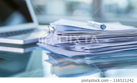 a stack of papers on a clear glass desk next to a laptop computer. a stack of papers on a clear glass desk next to a laptop computer. 116521242
