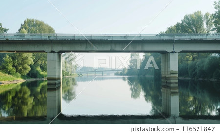 a concrete bridge crossing over a calm river. The sky is bright blue. 116521847