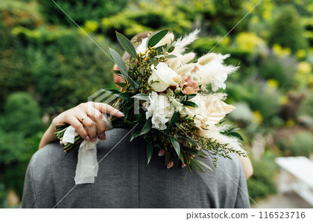 The bride and groom are hugging. The bride hugs the groom's neck and holds her bouquet of flowers 116523716