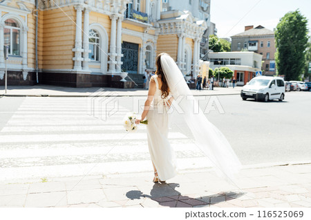 Wedding day. The bride walks along a city street in the sun. Her hair flutters beautifully in the wind Wedding day. The bride walks along a city street in the sun. Her hair flutters beautifully in the wind 116525069