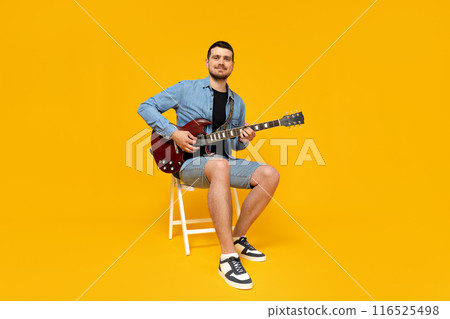 Attractive young guy with a guitar in his hands on a yellow background 116525498