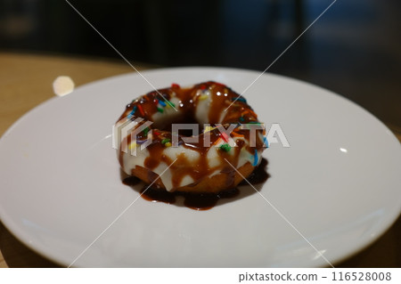 Donut with chocolate sauce and colorful sprinkles on a white plate 116528008