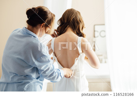 Bridesmaid is helping the bride to dress. Morning of wedding day 116528166