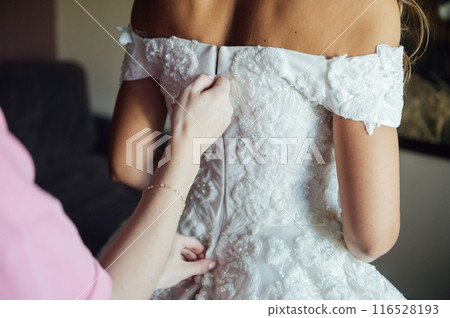 Bridesmaid is helping the bride to dress. Morning of wedding day Bridesmaid is helping the bride to dress. Morning of wedding day 116528193