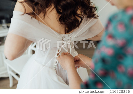Bridesmaid is helping the bride to dress. Morning of wedding day Bridesmaid is helping the bride to dress. Morning of wedding day 116528236