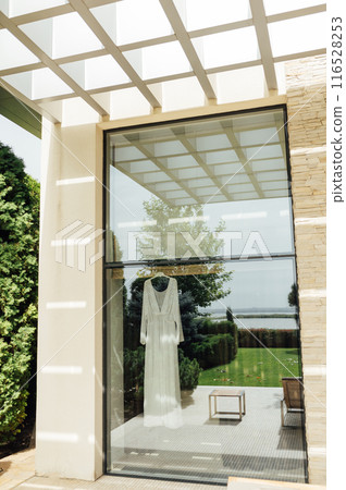 Beautiful wedding dress hanging near window on clothing rack in room Beautiful wedding dress hanging near window on clothing rack in room 116528253