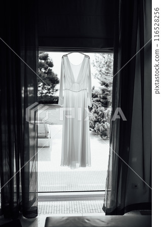 Beautiful wedding dress hanging near window on clothing rack in room Beautiful wedding dress hanging near window on clothing rack in room 116528256