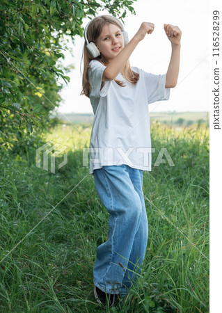 A child  with headphones listening to music and dancing in the park. 116528299