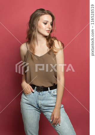 Stylish young adult woman in silk top wearing light jacket standing against red studio wall Stylish young adult woman in silk top wearing light jacket standing against red studio wall 116528519
