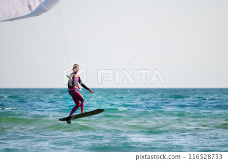 Young Caucasian woman athlete ride on a hydrofoil board with a kite in the open ocean. Hydrofoil is a new direction in kitesurfing 116528753