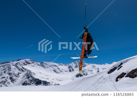 Freestyle skier performing a high jump with his skis crossed. High snow-capped mountains in the background Freestyle skier performing a high jump with his skis crossed. High snow-capped mountains in the background 116528865