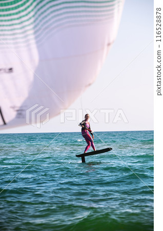young athletic woman skillfully jumps on a wave with a foilboard against the background of a clear sky in the turquoise sea 116528878