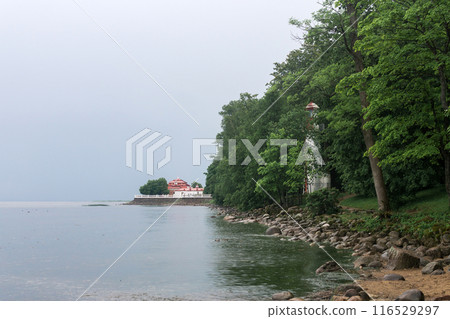 old lighthouse on the seashore among the trees against the backdrop of ancient buildings and embankment 116529297