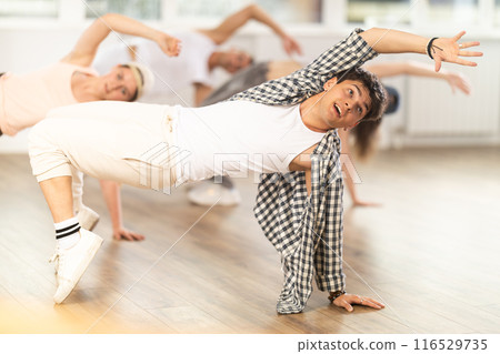 Man and his students perform hip hop dance on one bent leg, movement in horizontal plane near floor 116529735
