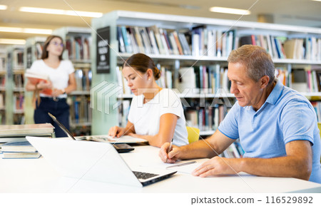 Mature man spending time in library, reading books and making laptop. Self-education concept Mature man spending time in library, reading books and making laptop. Self-education concept 116529892