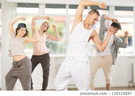 Young man standing performs basic hip hop movements in front of group of students 116529897