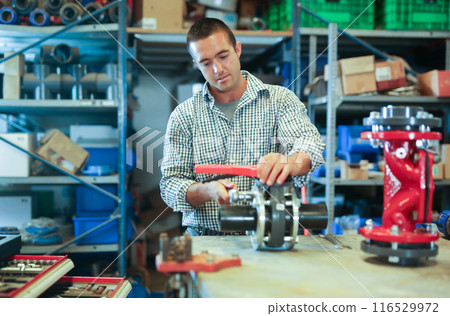 Factory worker assembles shutoff valves using various tools indoor Factory worker assembles shutoff valves using various tools indoor 116529972