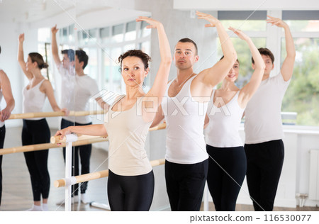 Group of positive young women and men engaged in classical ballet in dance studio performs exercise standing in 3rd position of ballet stance 116530077