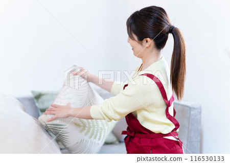 Middle-aged woman adjusting the cushions on the sofa 116530133
