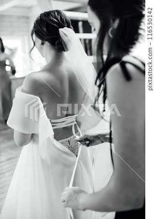 Bridesmaid is helping the bride to dress. Morning of wedding day Bridesmaid is helping the bride to dress. Morning of wedding day 116530142