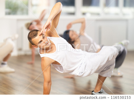 Man and his students perform hip hop dance on one bent leg, movement in horizontal plane near floor Man and his students perform hip hop dance on one bent leg, movement in horizontal plane near floor 116530153