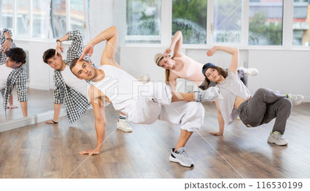 Man and his students perform hip hop dance on one bent leg, movement in horizontal plane near floor 116530199