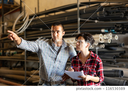 Man and woman working in warehouse, checking documents and poitning finger 116530389