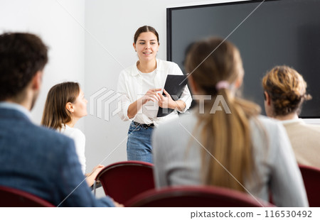 Portrait of young businesswoman standing near interactive board and participating in corporate seminar in auditorium Portrait of young businesswoman standing near interactive board and participating in corporate seminar in auditorium 116530492