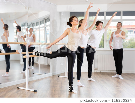 Woman mastering arabesque at barre during group ballet class 116530524