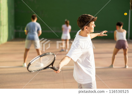 Guy hits the ball with a racket while playing frontenis on outdoor court 116530525