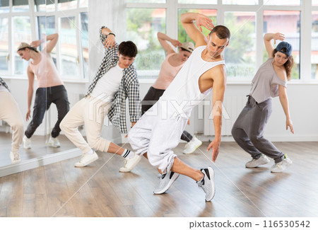 Young man standing performs basic hip hop movements in front of group of students 116530542