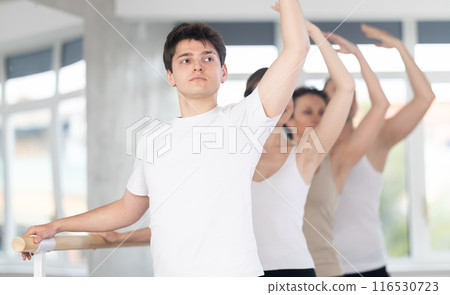 Group of dancers stand in third position at barre 116530723